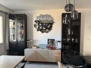 Um espaço de estar moderno com área de jantar, estante embutida, objeto decorativo na parede e uma cadeira preta.
