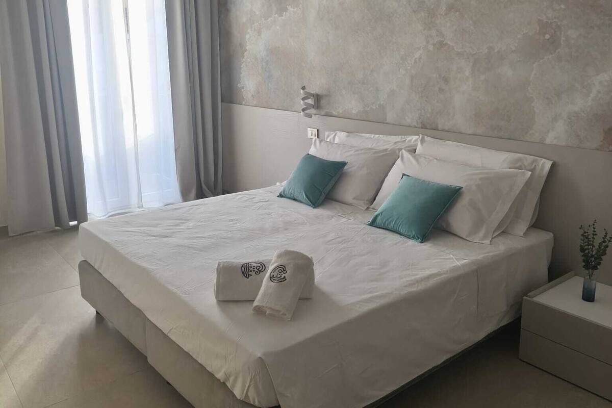 A modern bedroom with a large bed, a textured wall, and a nightstand with a vase.