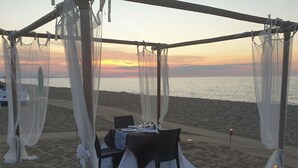 Een eettafel met stoelen onder een overkapping aan het strand, met uitzicht op zee.