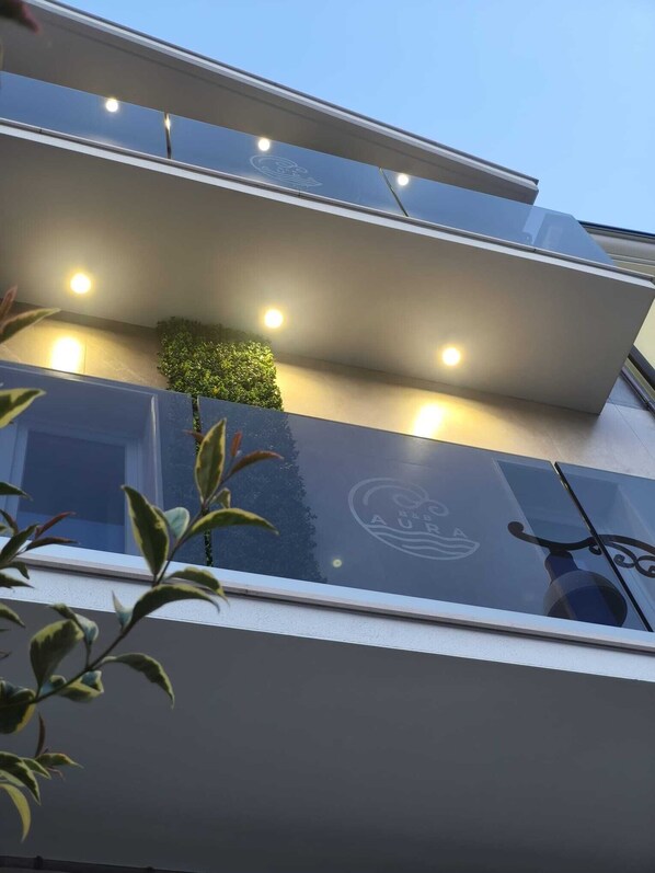 A modern building with a glass facade, recessed lighting, and a small green plant on the balcony. - B&B Aura (Lesina)