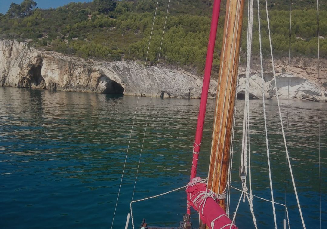 En sejlbåd med en klippefyldt kystlinje i baggrunden.