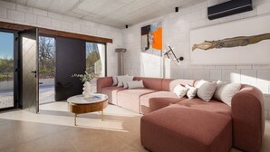 Een moderne woonkamer met een roze modulaire bank, een ronde salontafel en een groot raam met uitzicht op de natuur.