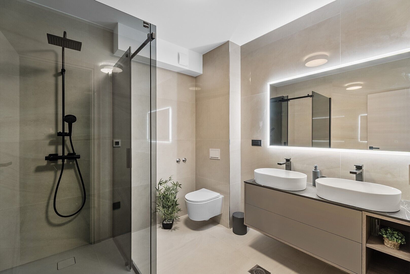 A modern bathroom with a glass-enclosed shower, a toilet, and a vanity with two sinks and a large mirror.