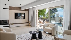 Una sala de estar moderna con televisor de pantalla plana, asientos cómodos y vista a un área de piscina al aire libre.
