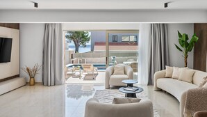 Una sala de estar moderna con un televisor grande, un sofá, una mesa de centro y vistas a una zona de piscina al aire libre.