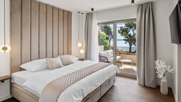 Un dormitorio moderno con una cama grande, vistas al mar y un balcón con mobiliario exterior.