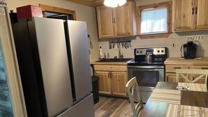 Una cocina compacta con armarios de madera, un refrigerador de acero inoxidable, una estufa y una cafetera.