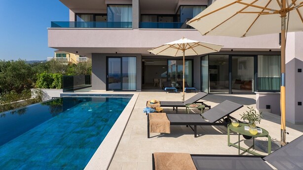 Una casa moderna de dos pisos con piscina, mobiliario exterior y una gran sombrilla.