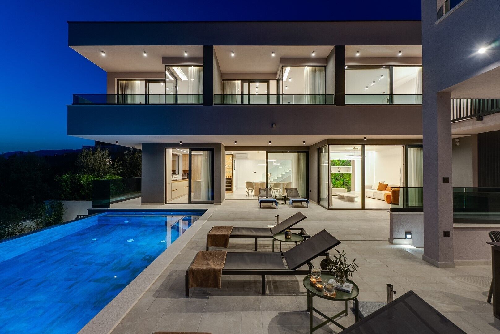 Une maison moderne à deux étages, dotée d’une piscine, d’un espace salon extérieur et de grandes fenêtres.