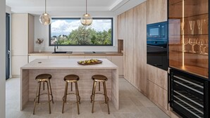 Cocina moderna con una isla grande, taburetes de bar, luces colgantes y vistas a zonas verdes.