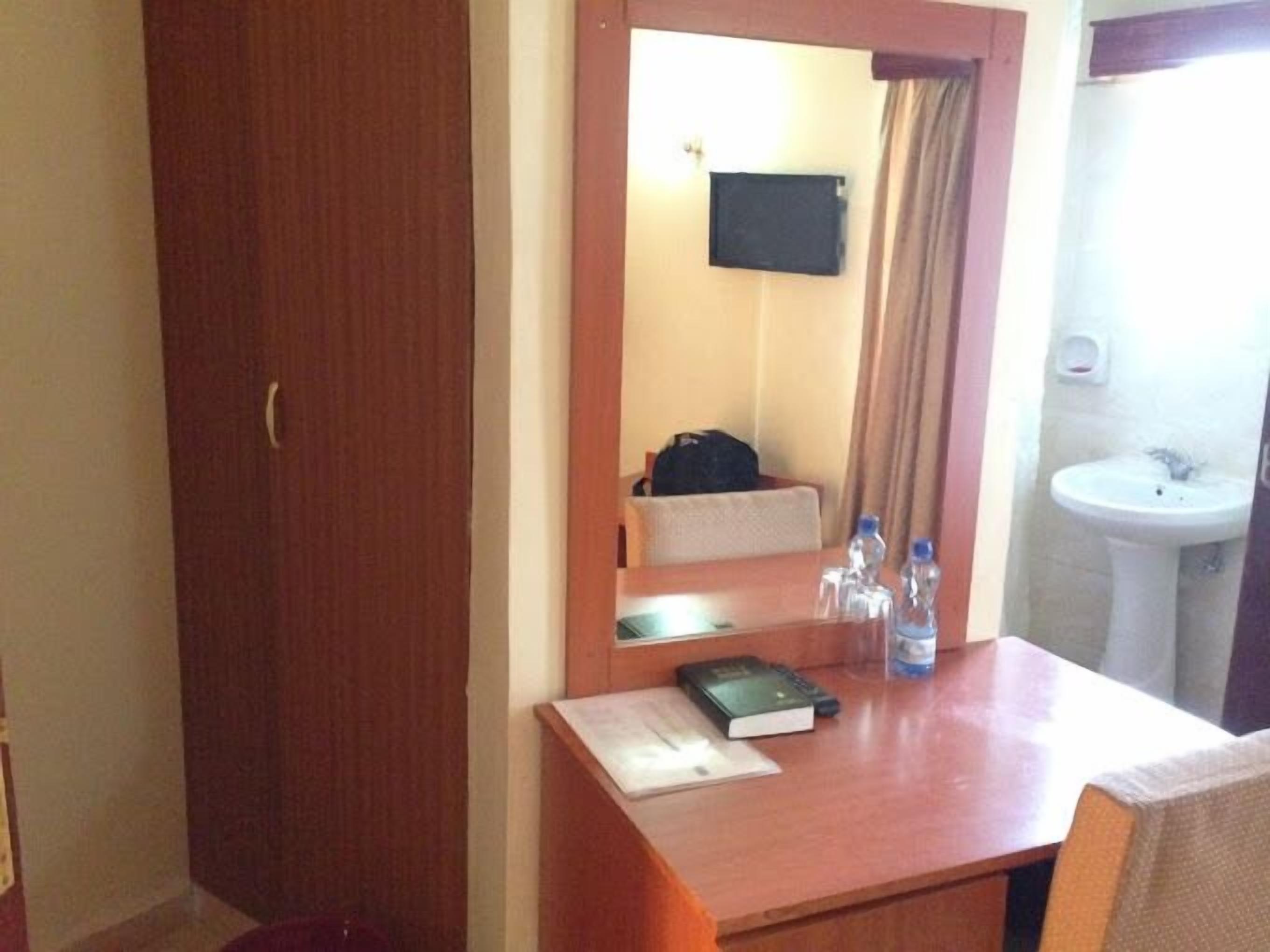 Habitación de hotel con un escritorio de madera, un espejo, un lavamanos pequeño y un perchero para toallas.