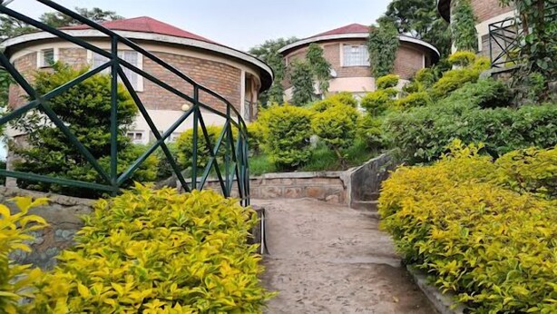 A pathway leading to a building with a curved roof, surrounded by lush greenery and yellow foliage. - ACK Guest House Homabay (Homa Bay)