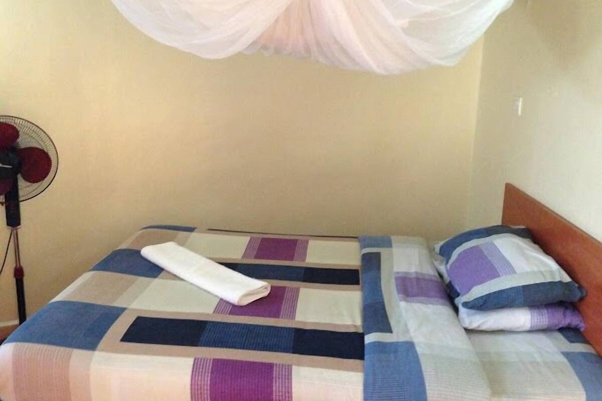 A bed with a checkered bedspread, a white towel, and a wooden headboard.