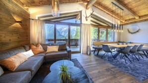A modern interior with a wooden ceiling, a sectional sofa, a dining area with chairs, and large windows offering mountain views. - Chalet Near Slopes, Sleeps 6 (Neukirchen am Grossvenediger)