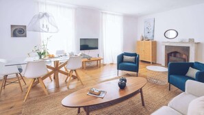 A modern living room with a glass dining table, blue armchairs, and a fireplace.