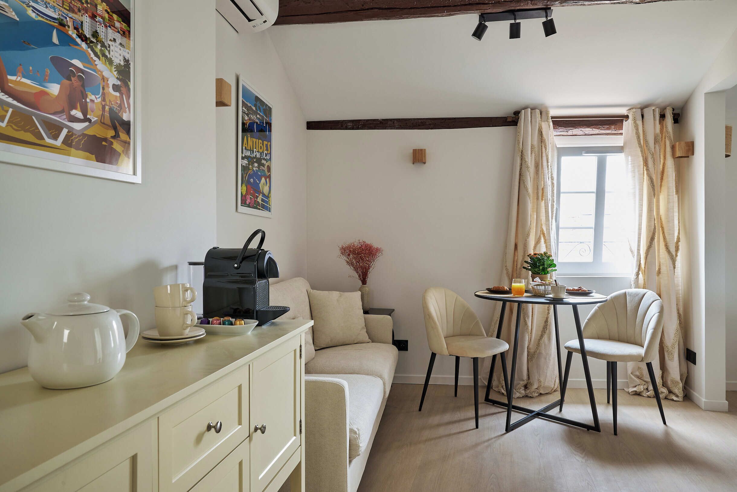 Une pièce confortable avec un canapé, une table à manger et des chaises, un coin café et une fenêtre avec des rideaux.