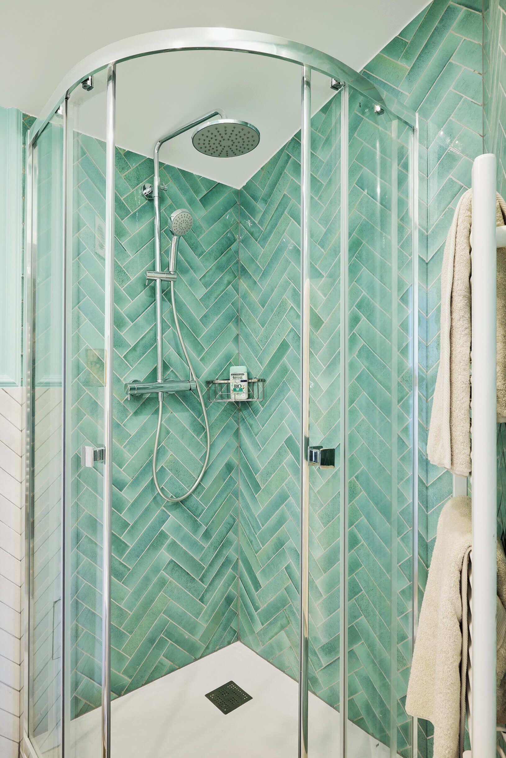 A glass-enclosed shower with a herringbone tile pattern and a handheld showerhead.