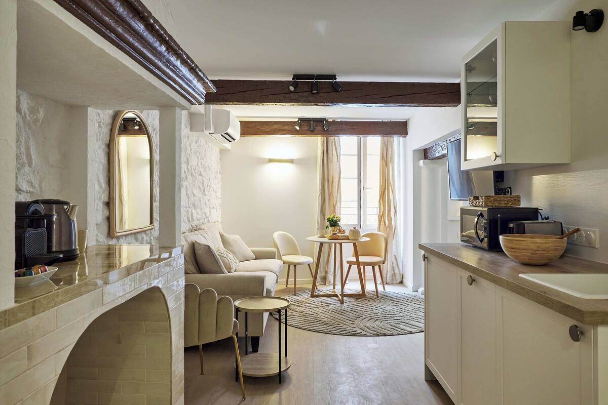 Une cuisine moderne dotée d’un four encastré, un coin repas avec une table ronde et des chaises, et un espace salon confortable avec un canapé et des fauteuils.