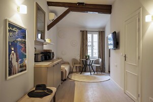 A compact living space with a kitchenette, a dining area with a table and chairs, a television mounted on the wall, and a large poster on the wall.