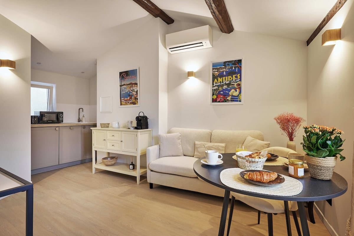 Un salon moderne avec un canapé, une table à manger où sont disposés des aliments pour le petit-déjeuner, une cuisine en arrière-plan et des œuvres d’art décoratives accrochées au mur.