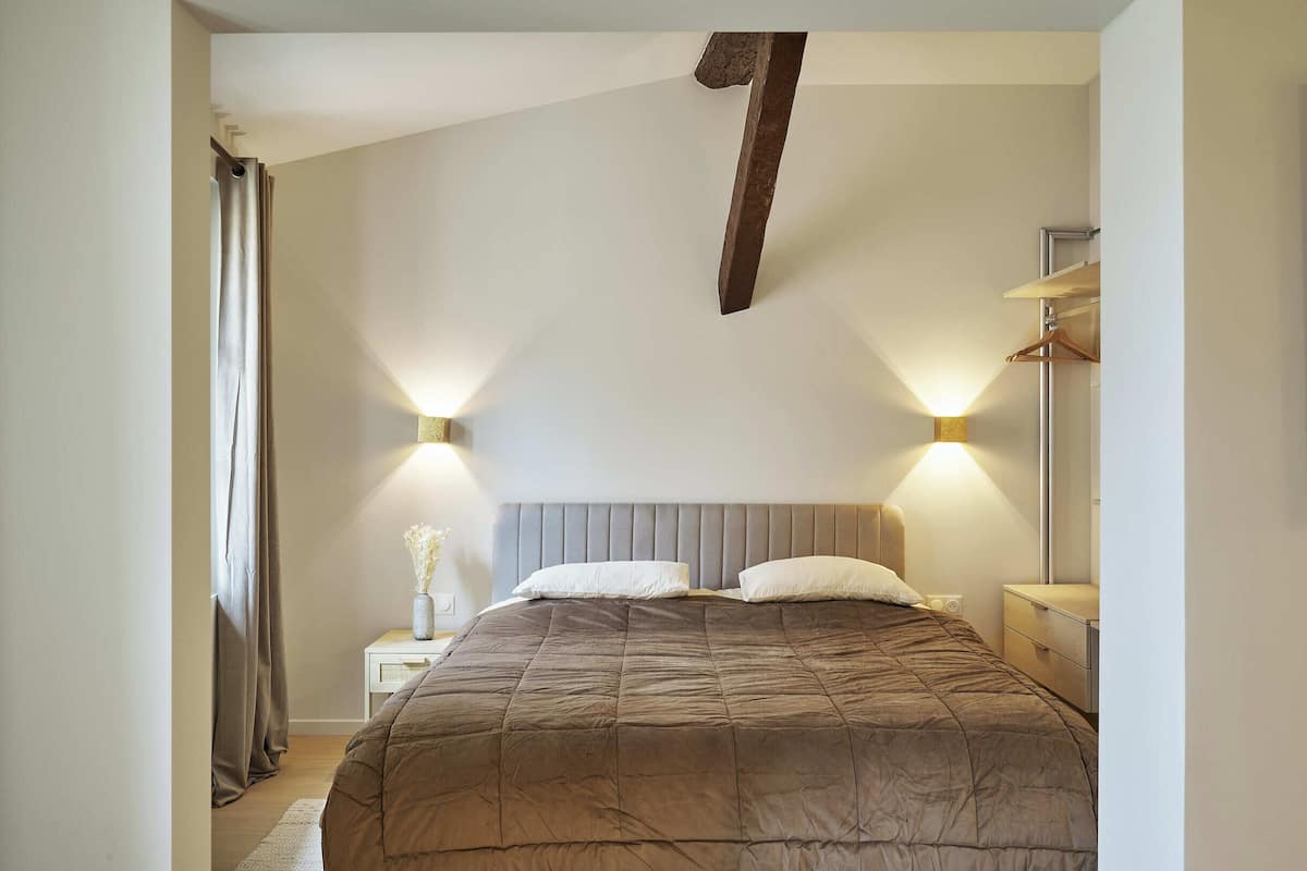 Une chambre à coucher avec un grand lit, deux lampes de chevet, une table de chevet, une commode et un luminaire suspendu.