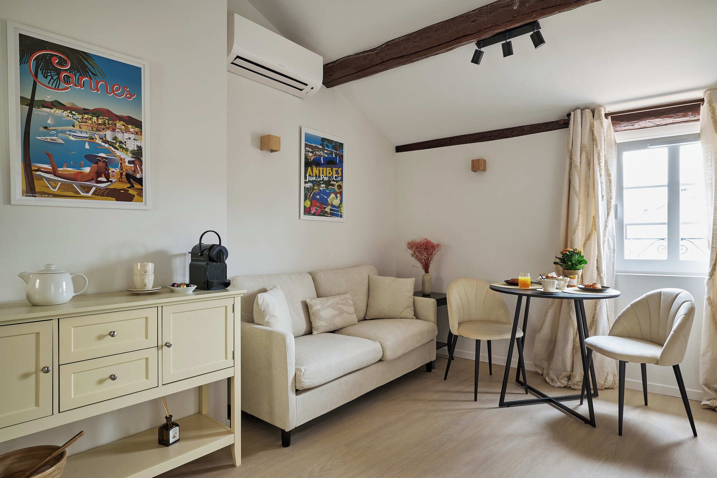 Ein gemütliches Zimmer mit einer Couch, einem kleinen Tisch und einem Sessel. An der Wand hängt ein Bild und auf dem Regal eine Uhr.