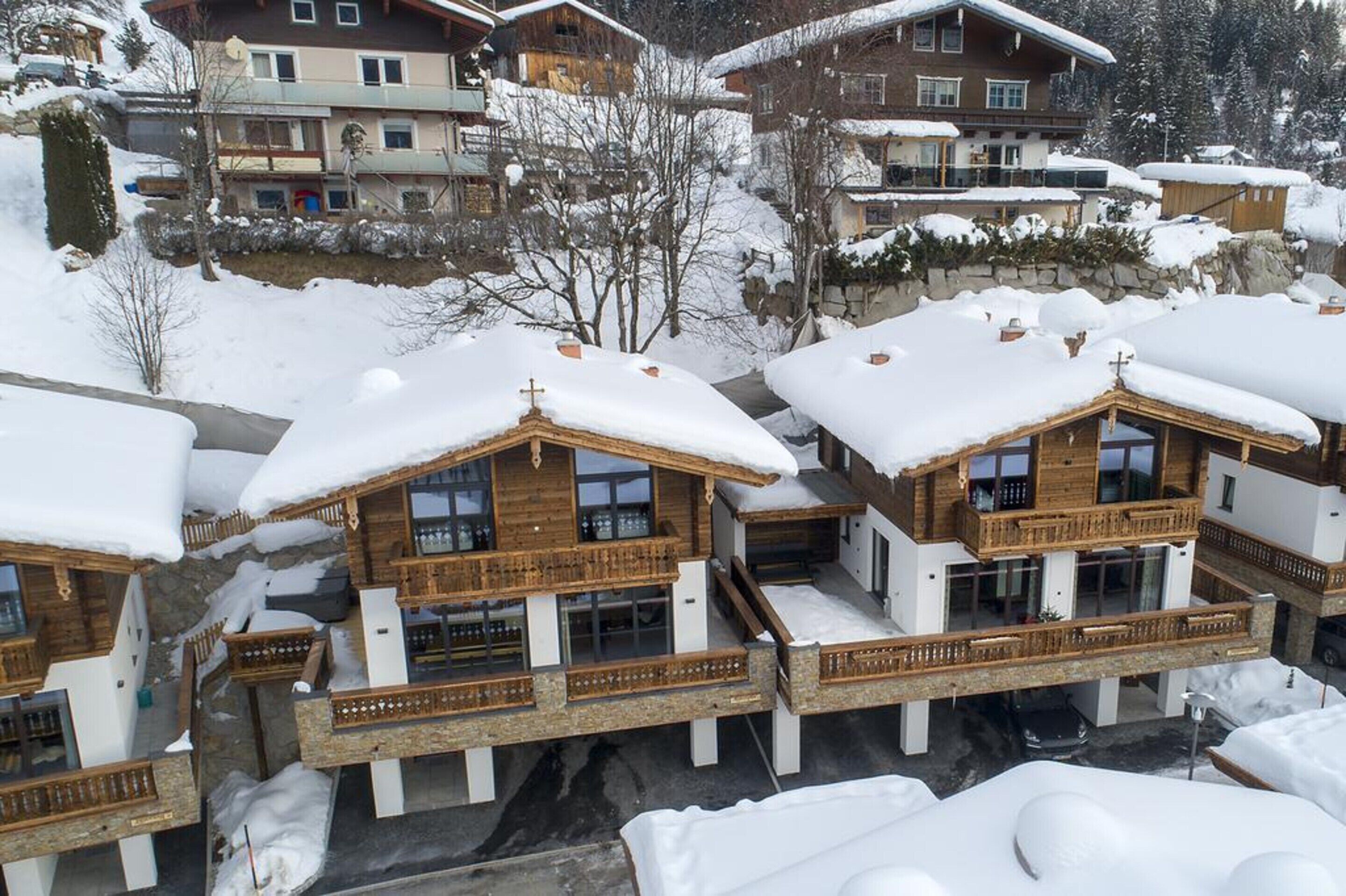 A cluster of wooden chalets with balconies, set in a snowy mountainous area.
