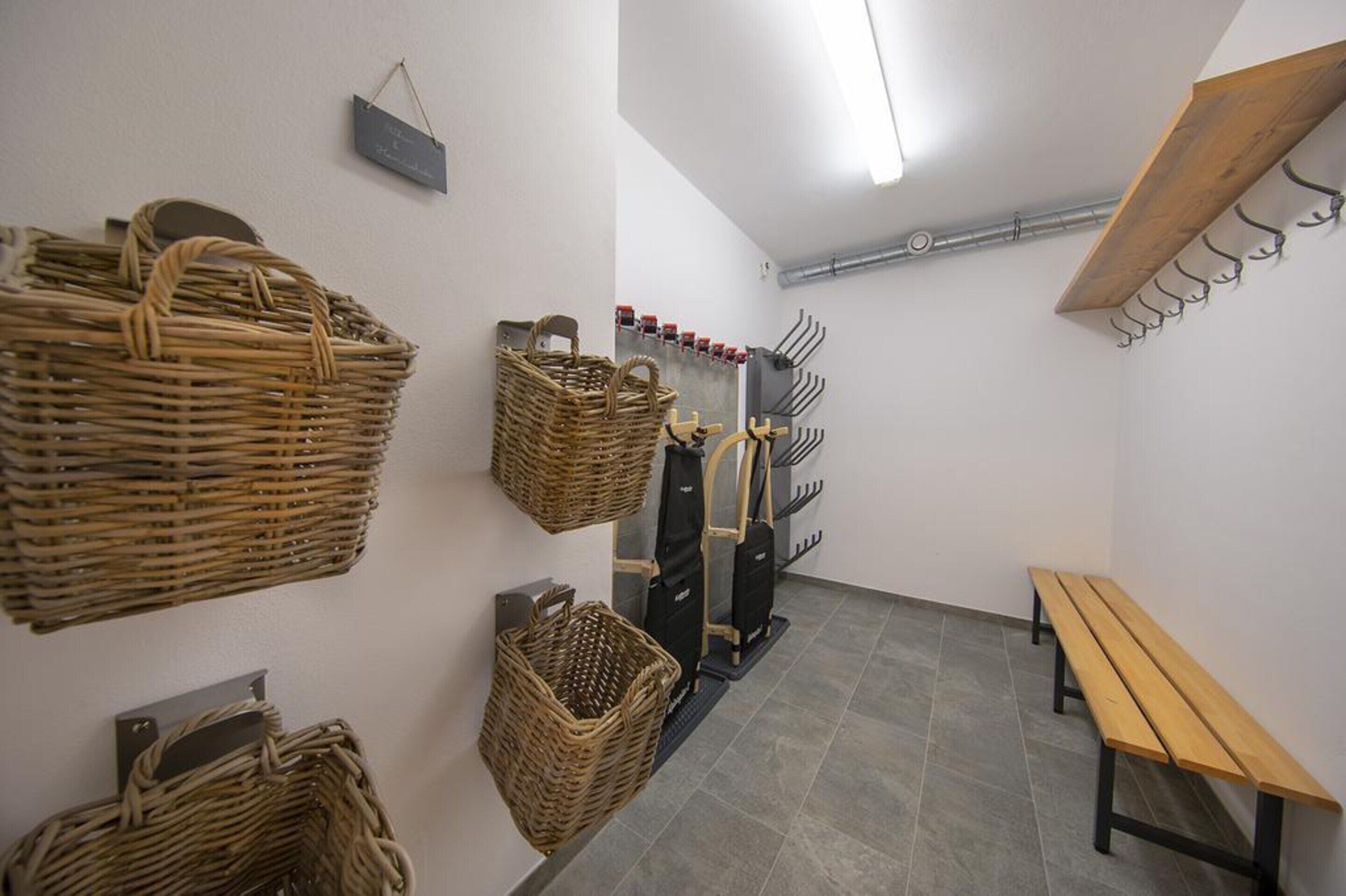 A room with wicker baskets on the wall, a bench, and a coat rack.