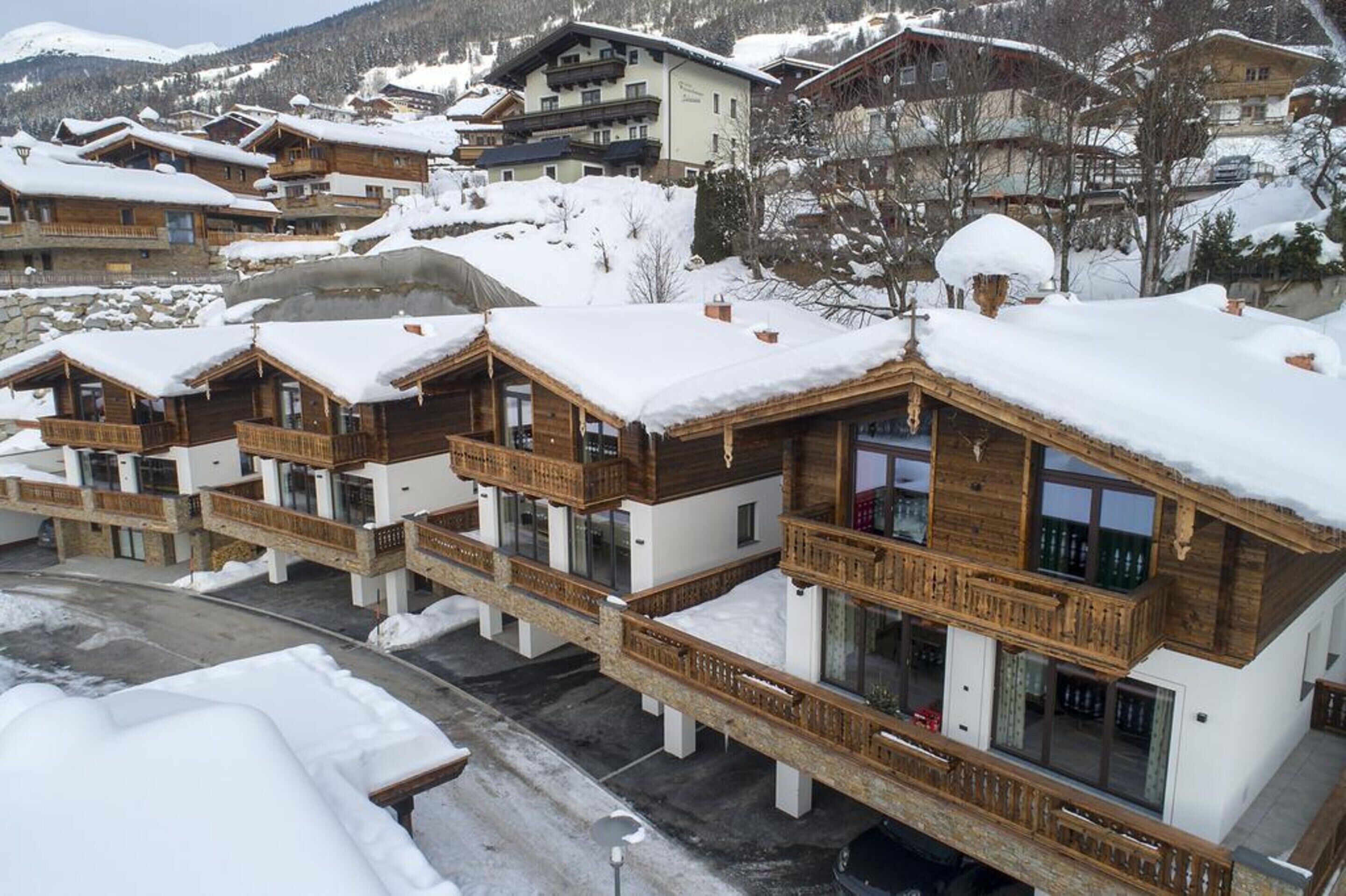 A row of wooden chalets with balconies, set against a snowy mountain backdrop.