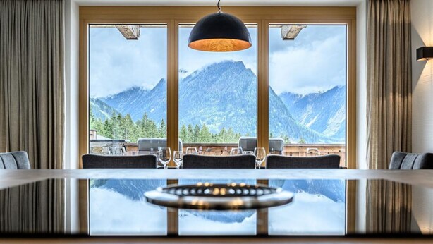 Un coin repas avec une table et des chaises, de grandes fenêtres offrant une vue sur les montagnes et un luminaire suspendu.