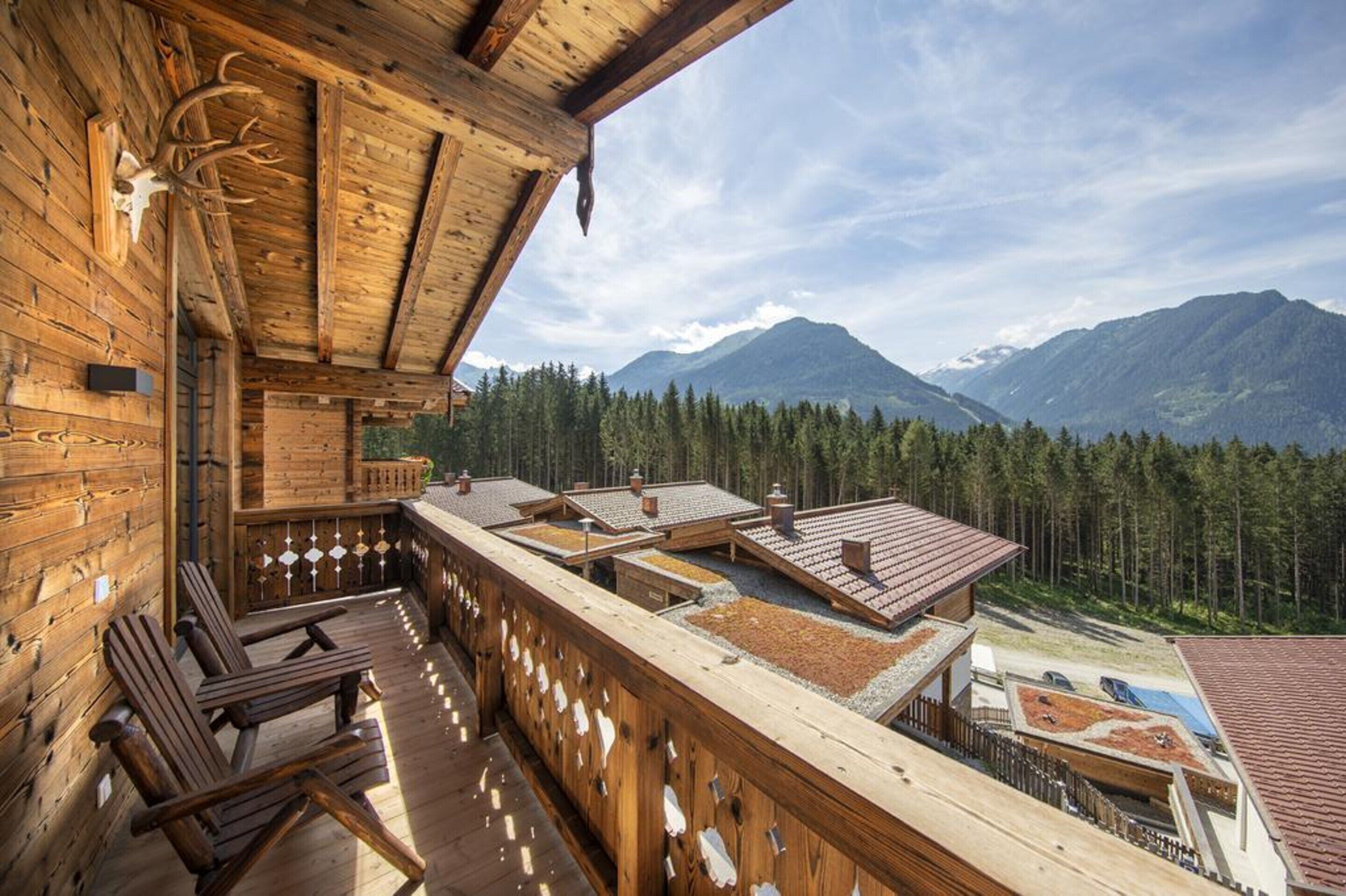 A wooden cabin with a balcony overlooking a forest and mountains.