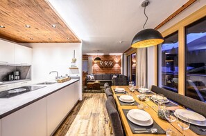 A modern kitchen with a wooden ceiling, a dining area with a long table set for a meal, and a cozy seating area with a fireplace. - Family Chalet Escape in the Alps (Neukirchen am Grossvenediger)