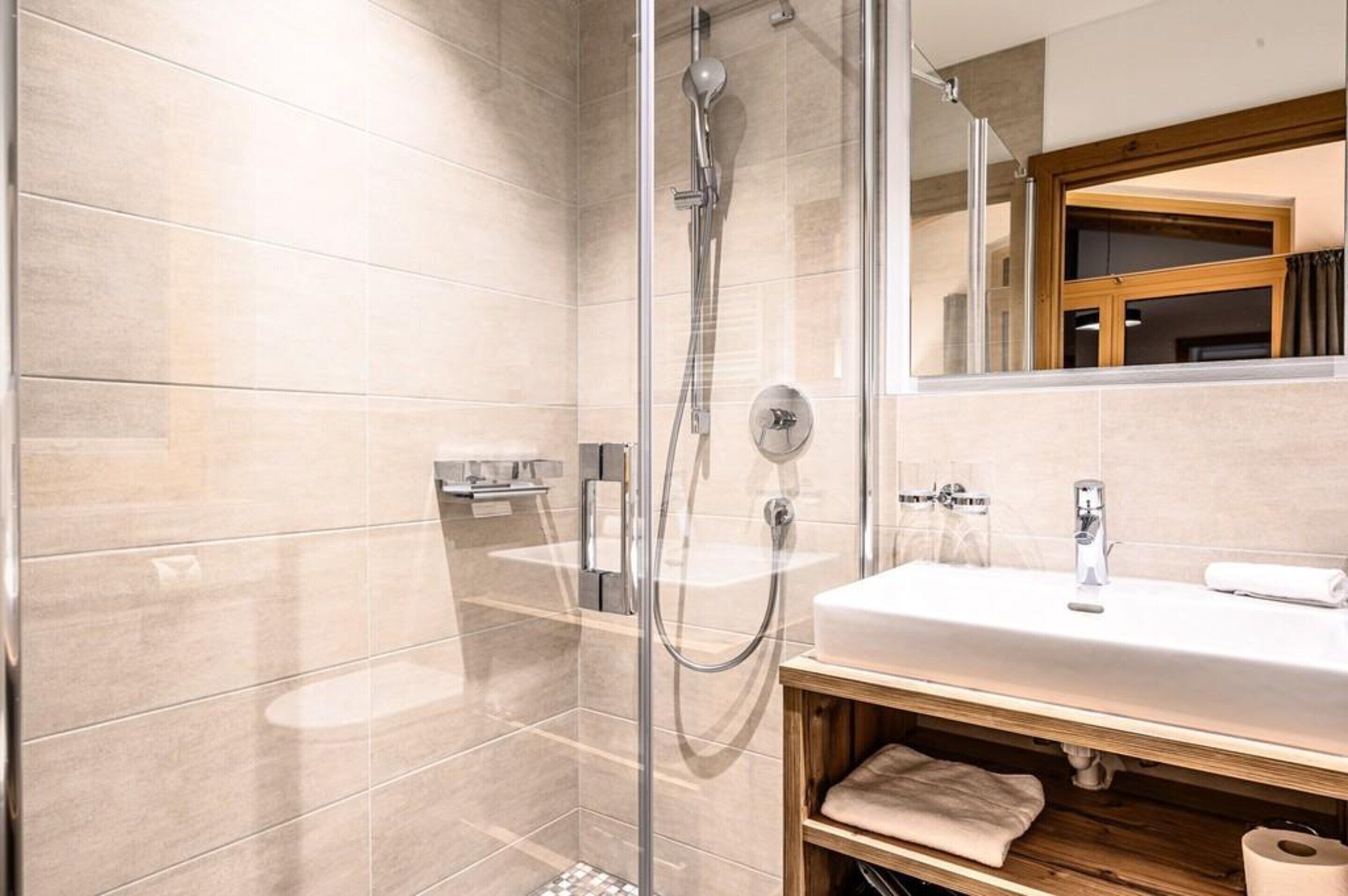 A modern bathroom with a glass-enclosed shower, a white sink, and a wooden vanity.