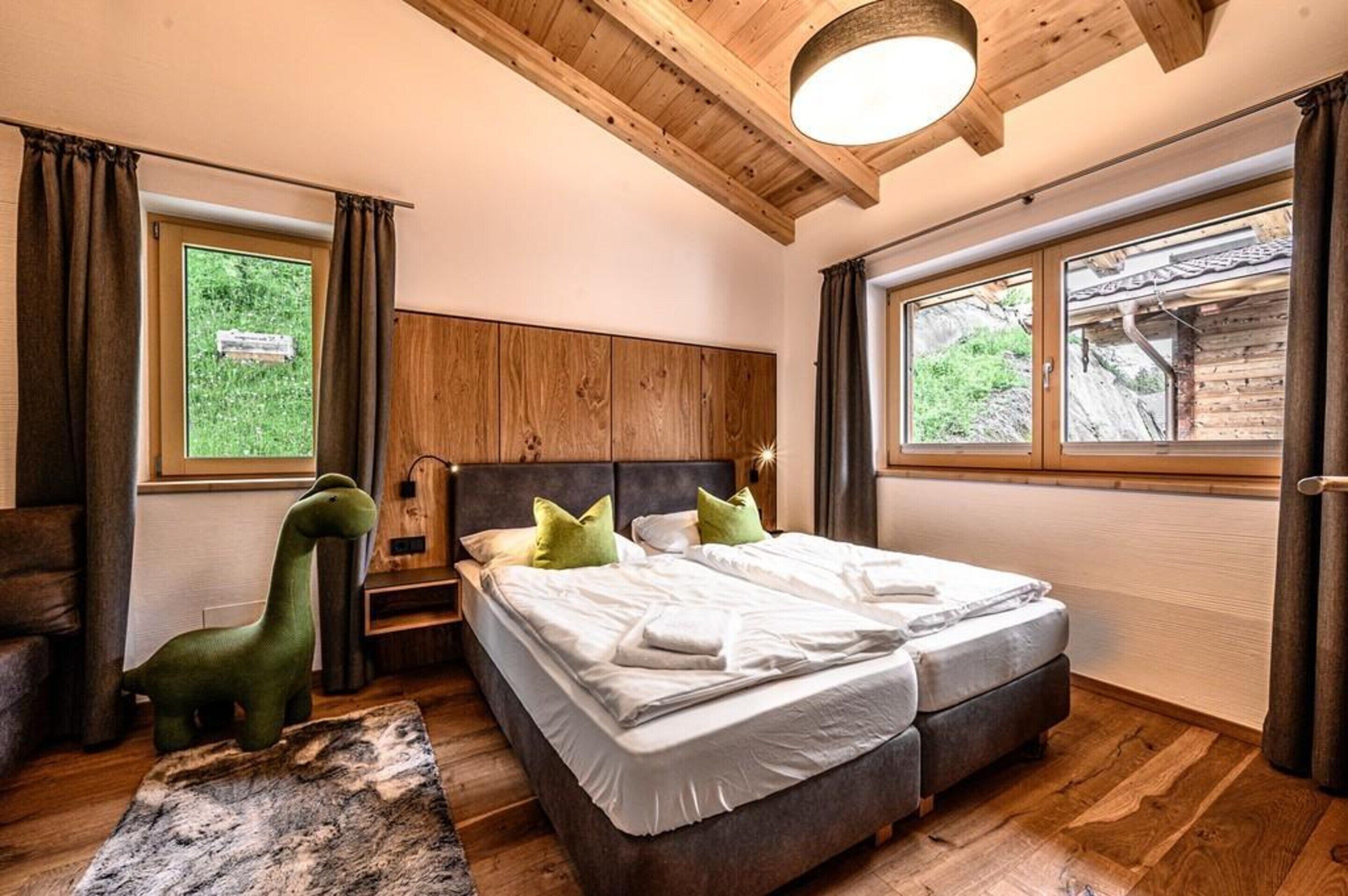 A bedroom with two beds, wooden headboard, large windows, and a small dinosaur toy.