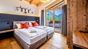 Une chambre avec deux lits, des poutres apparentes en bois au plafond, une grande fenêtre donnant sur les montagnes et une porte-fenêtre coulissante.