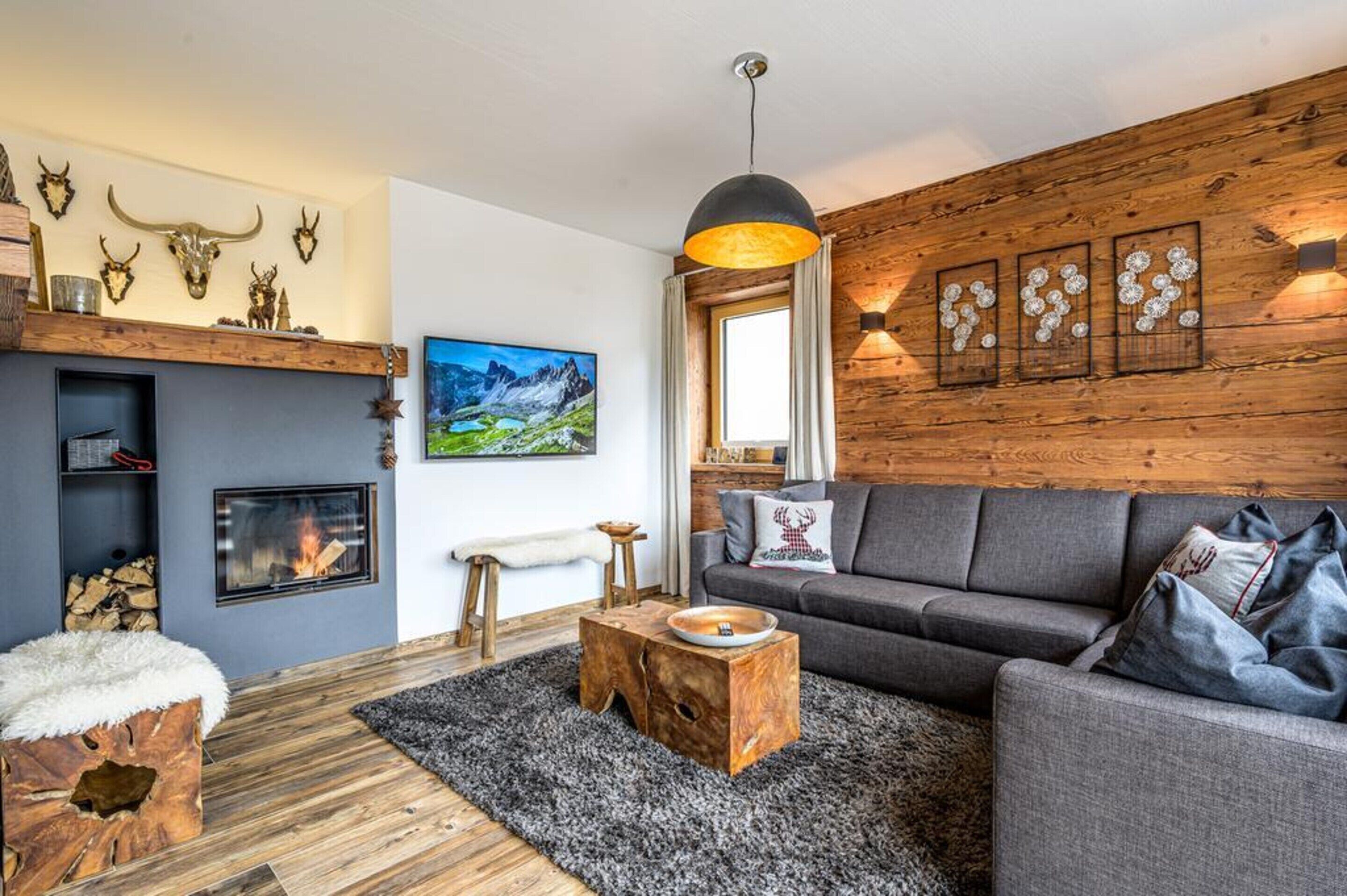 En hyggelig stue med pejs, en grå sofa, trædekorationer på væggen og et stort vindue.