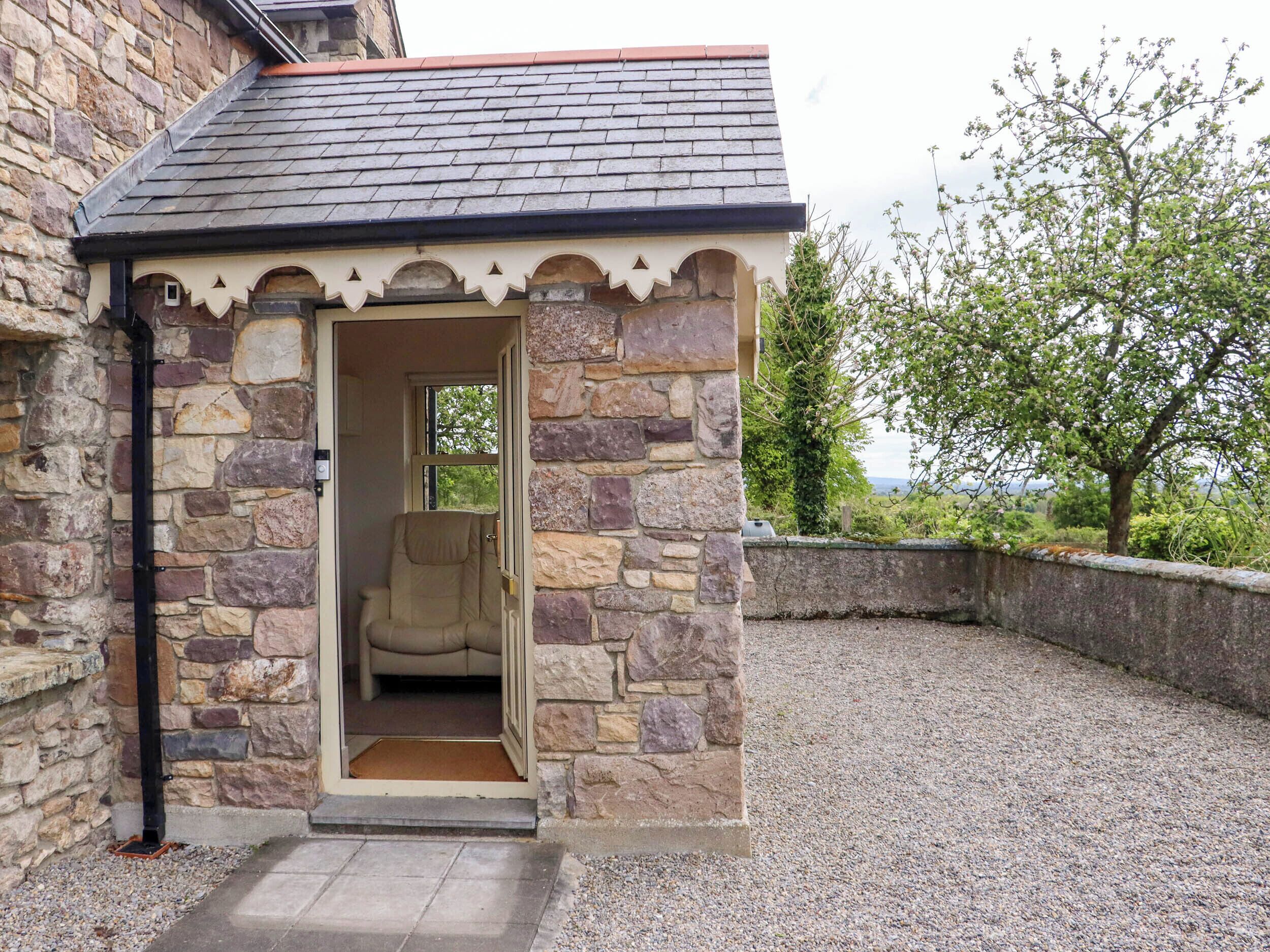 A stone building with a door leading to a beige chair, surrounded by gravel and greenery.