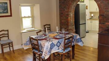 A dining area with a brick archway, wooden chairs, a table set with plates and glasses, and a window with blinds.