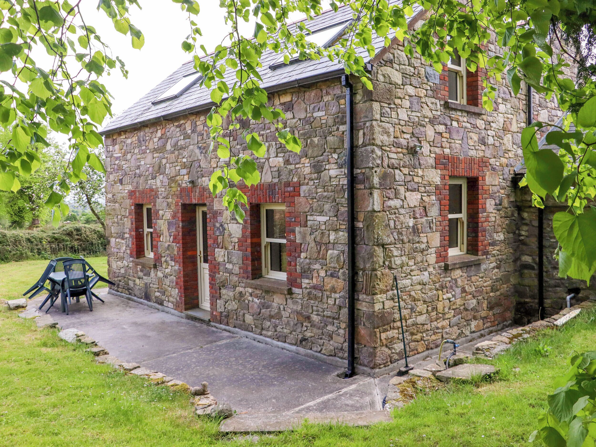 A stone building with a sloped roof, a paved driveway, and a small outdoor seating area with chairs.