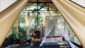 A tent with a bed, a table, and potted plants. - Mây Glamping (Xuan Truong - Da Lat)