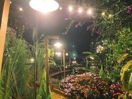 Um jardim com diversas plantas e flores, iluminado por luzes pendentes.