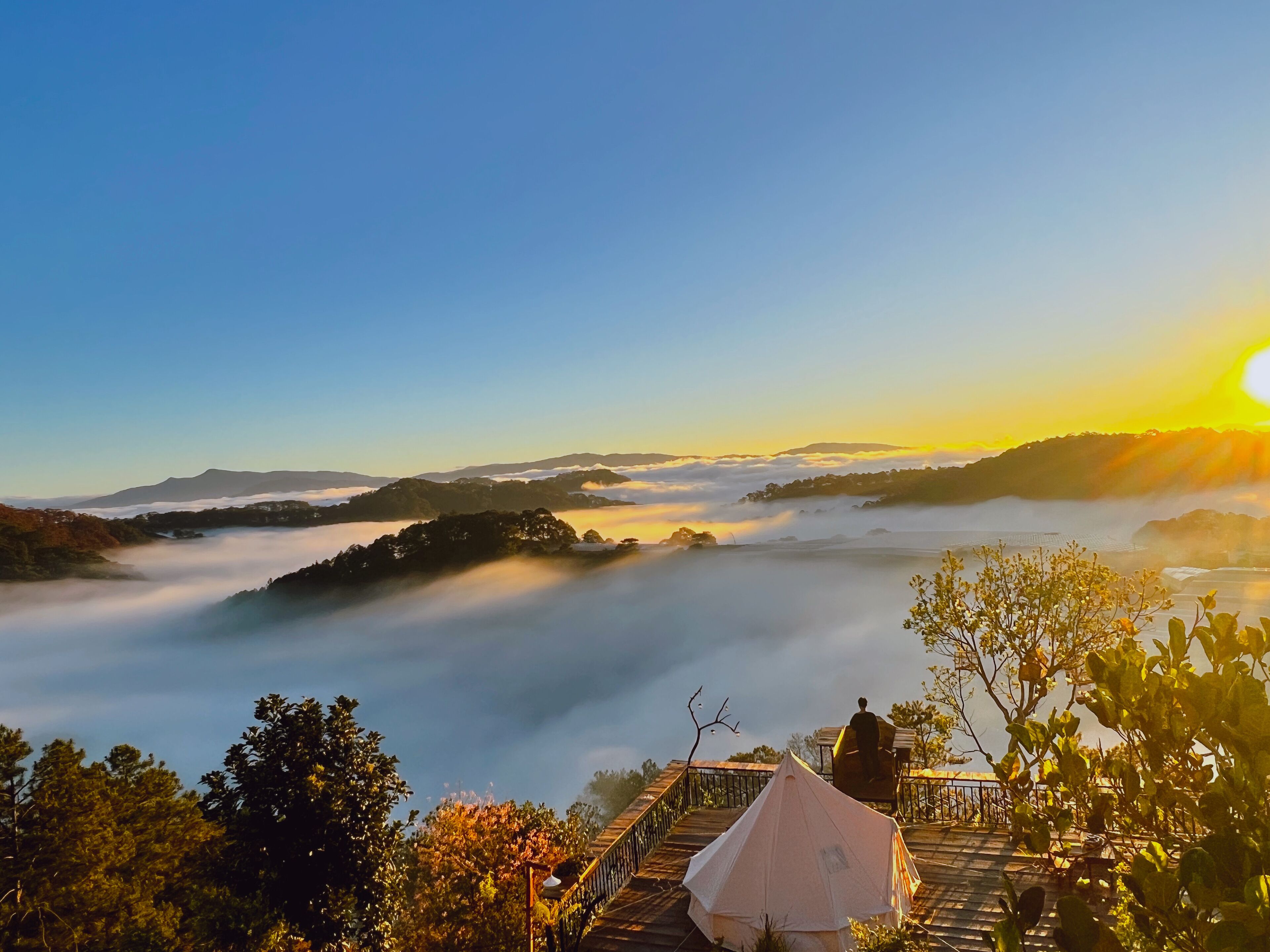 A high vantage point with a clear view of a valley, a wooden deck, and a tent.