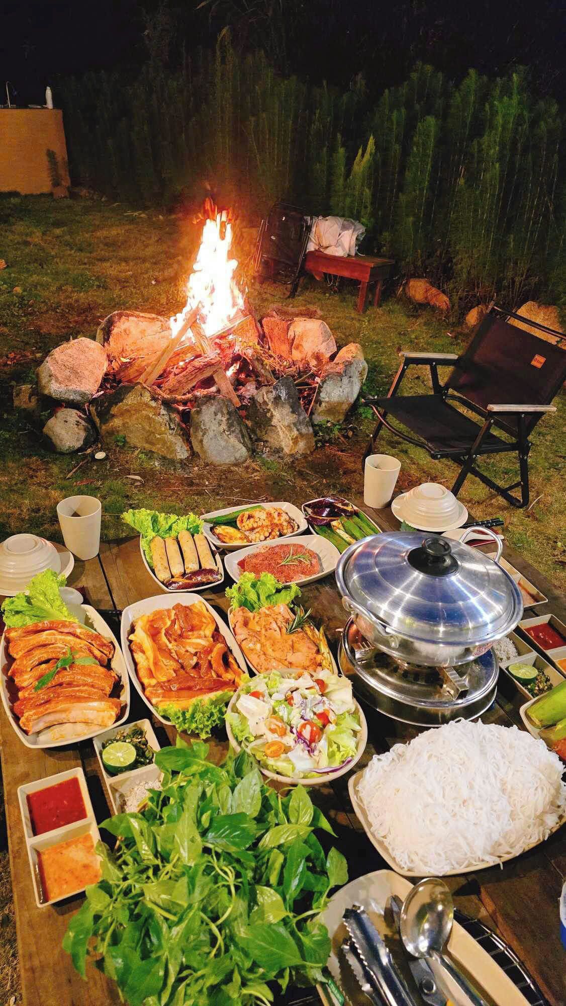 An outdoor dining setup with a fire pit, various dishes, and a table with utensils.