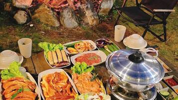 An outdoor dining setup with a fire pit, various dishes, and a table with utensils.