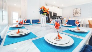 Ein Esstisch ist gedeckt mit weißen Tellern, blauen Platzsets und klarem Glas mit orangefarbenen Blumen.