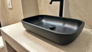 Ein modernes Badezimmer mit einem eleganten, schwarzen Waschbecken, einem Wasserhahn und einem Lichtschalter an der Wand.