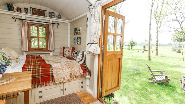 Ein gemütliches Schlafzimmer mit großem Fenster, Holztür und Blick auf eine Rasenfläche mit einer Bank.