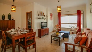 A living room with a dining area, a sofa, a television, and a window with curtains.