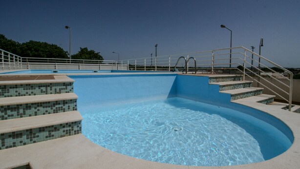 A swimming pool with clear blue water, steps leading into the pool, and a metal railing around the perimeter.