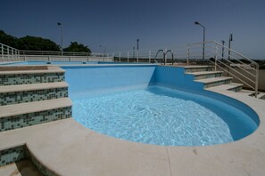 A swimming pool with clear blue water, steps leading into the pool, and a metal railing around the perimeter. - FLH Armação de Pêra Homey Apartment (Armação de Pêra)